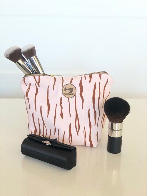 Deze afbeelding toont een openstaande cosmetische tas die gevuld is met diverse make-upkwasten. De tas ligt op een houten tafel. De kwasten zijn van verschillende soorten en maten, waaronder kwasten voor poeder, blush, foundation en oogschaduw. De afbeelding is goed belicht en de kleuren zijn helder.