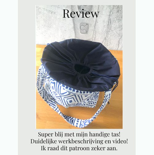 "Een foto van een blauwe en witte bucket bag met een trekkoord. De tas is gemaakt van een stevige stof met een geometrisch patroon. De tas ligt op een houten tafel en er ligt een review op papier naast. De review luidt: 'Super blij met mijn handige tas! Duidelijke werkbeschrijving en video! Ik raad dit patroon zeker aan.'"